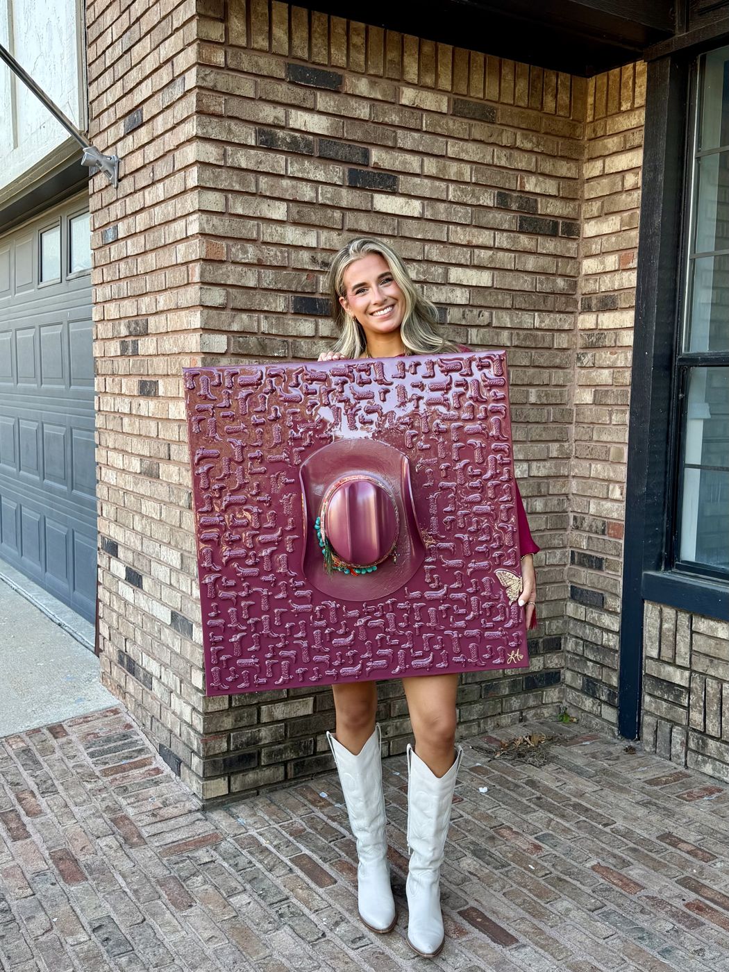 A woman in white boots holding a berry canvas covered in tiny boots with a matching cowboy hat