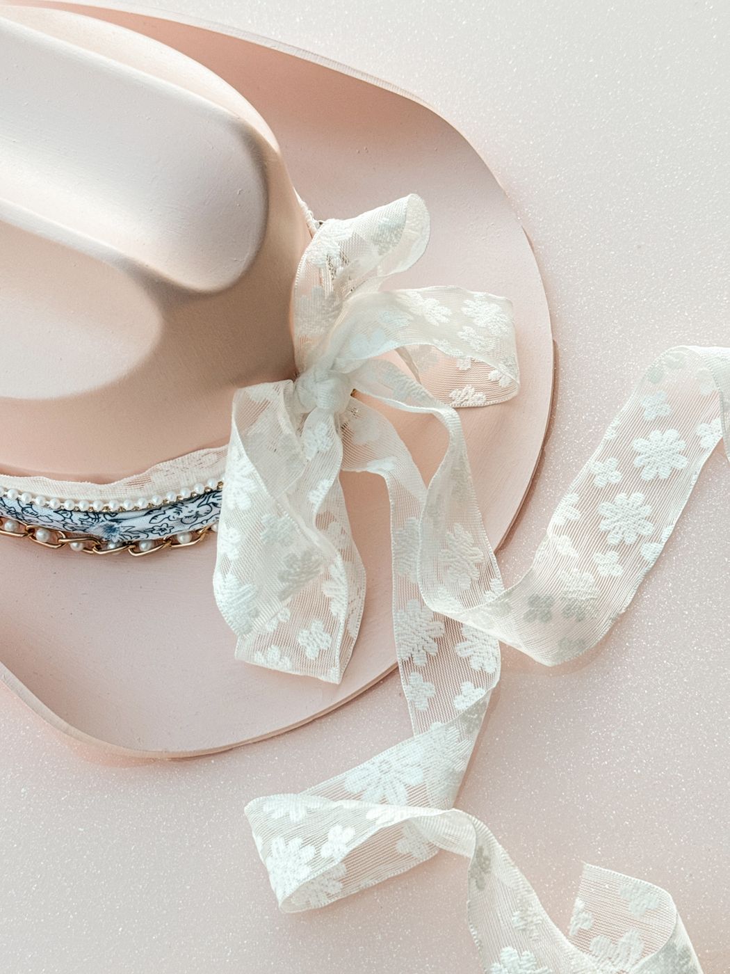 Close-up of a blush cowboy hat with a pearl and jewel hat band and lace ribbon